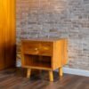 Enhance your space with The Single Drawer Teak Nightstand, featuring solid teak wood, natural satin finish, and a practical open drawer design.